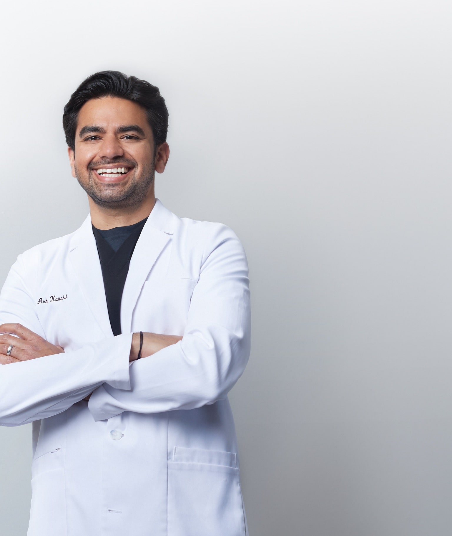 A male Renovo Endodontist smiles at camera in a scrubs shirt with his office blurred in the background.