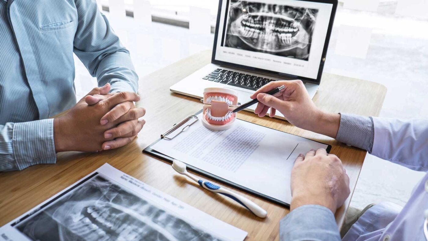 A dentist explaining treatment options using a dental model and X-rays