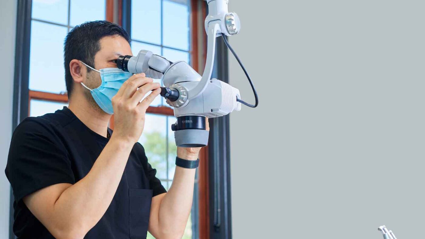 A masked medical professional uses a microscope for a procedure.