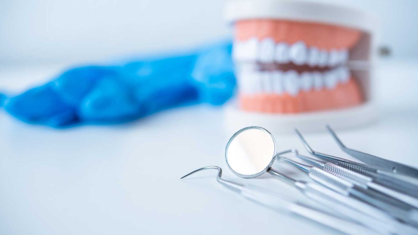 Dental tools with a model of teeth and blue gloves in the background