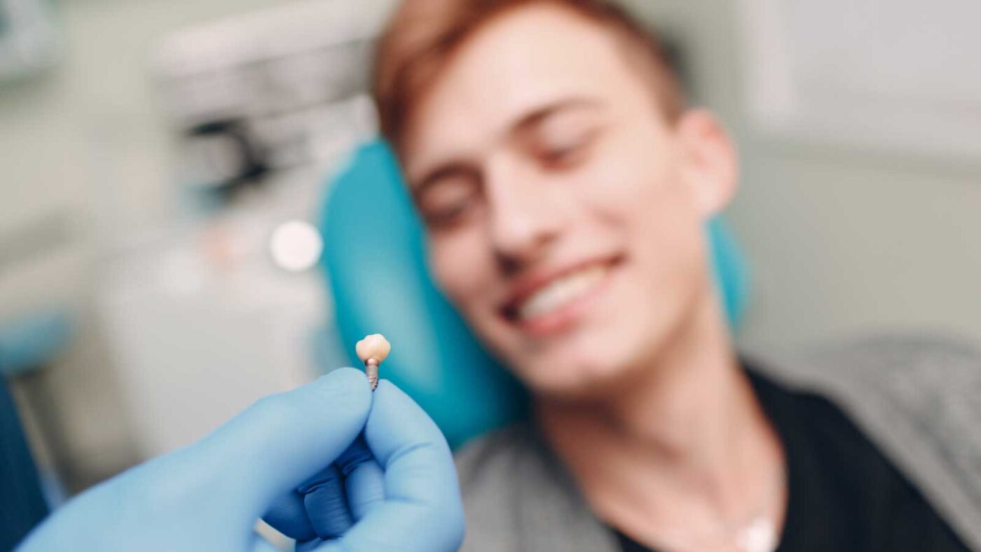 Dentist holding a dental implant while a smiling patient looks on