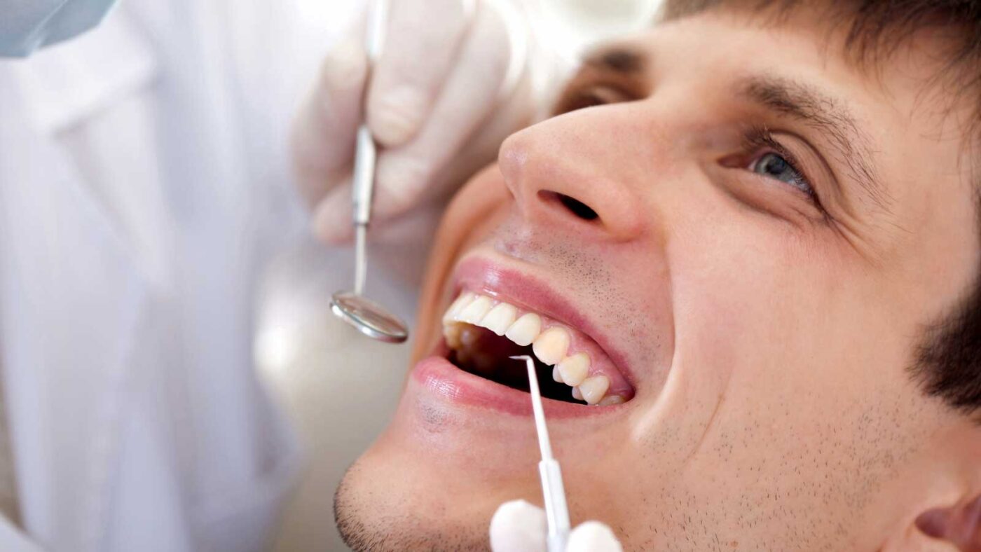 Man smiling during a dental check-up with tools in his mouth