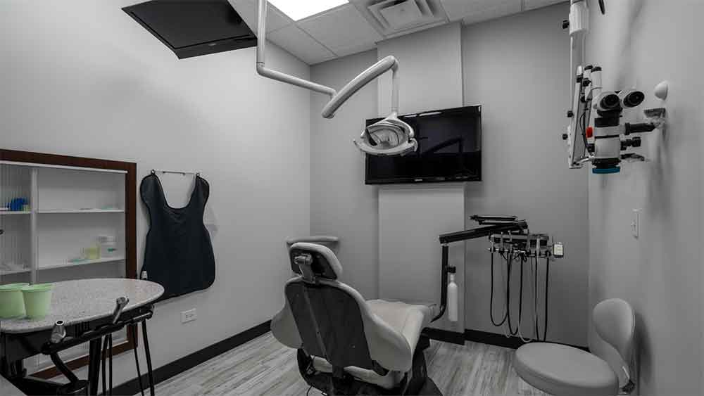 A modern dental examination room with a chair, overhead light, and medical equipment.