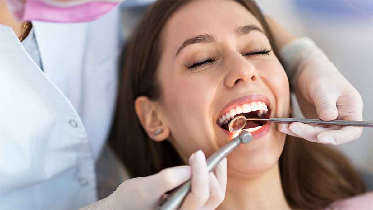 A smiling woman receives a dental checkup from a gloved dentist.