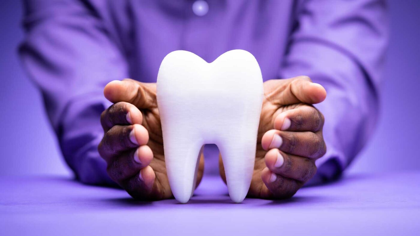 Hands holding a large model of a tooth on a purple background.