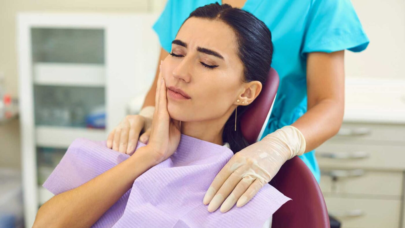 Woman in dental chair holding cheek in pain.