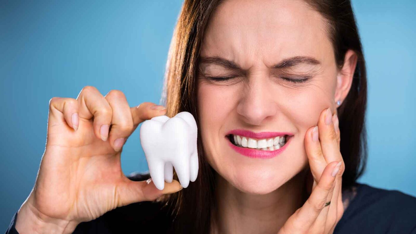 Woman with tooth pain holding a model tooth