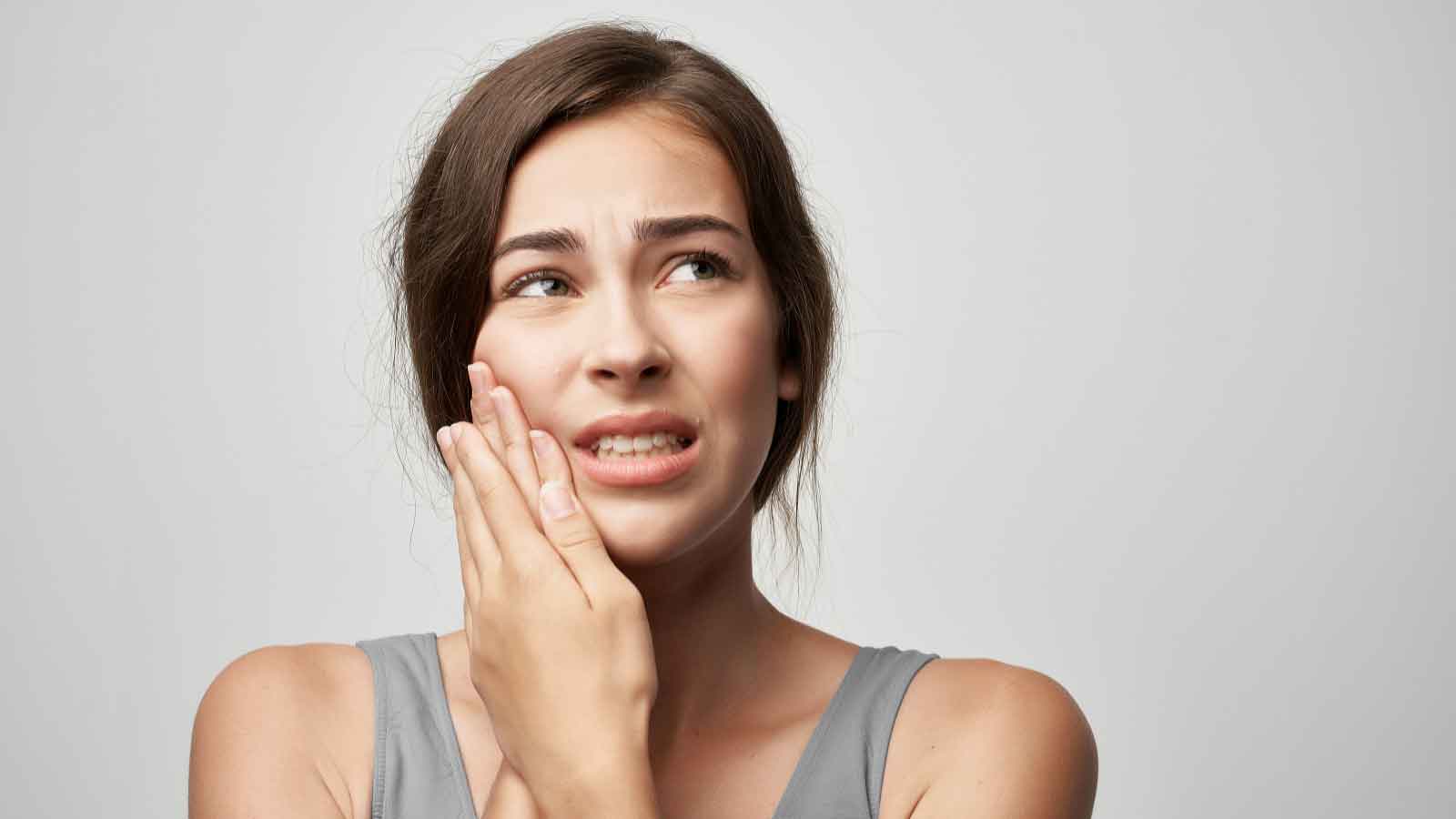 A-woman-grimacing-in-pain,-holding-her-cheek