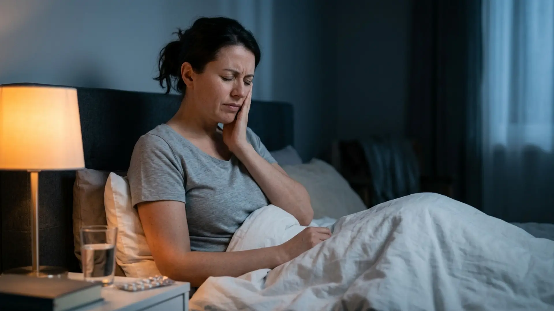 Woman experiencing tooth nerve pain at night while sitting in bed.
