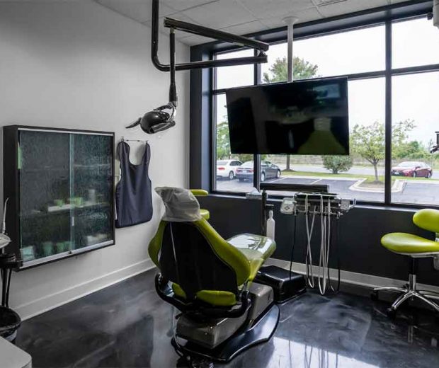 Modern dental exam room with a green chair and large window.